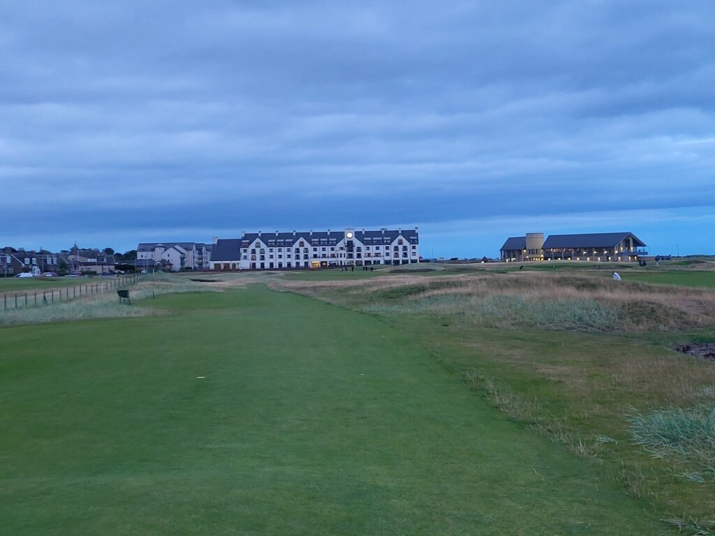 Looking up the 18th fairway at Carnoustie at dusk toward the hotel and the clubhouse, with the rough and the burn to the right and a heavy Scottish sky above